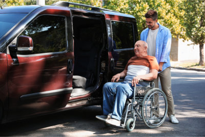 Young men helping patient in wheelchair to get into van outdoors